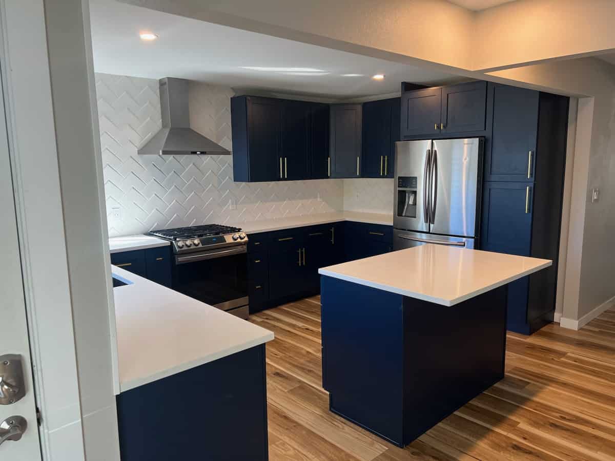 Side view of a newly renovated kitchen in Denver with blue cabinets, blue island, white walls, and new wood flooring